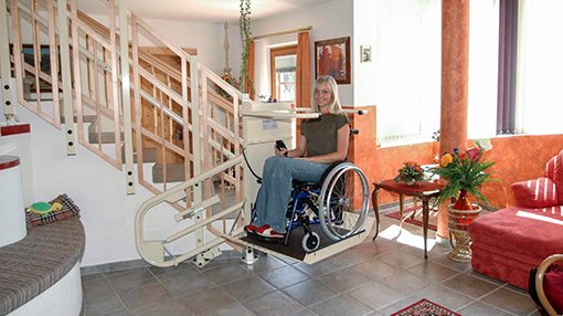 Eine junge Dame benutzt mit ihrem Rollstuhl den Plattformtreppenlift OMEGA im Innenbereich
